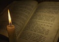 Burning candle illuminates the defocused unfolded pages of an old book