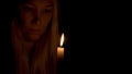 A burning candle illuminates the face of a beautiful young woman in the dark.