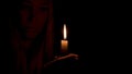 A burning candle illuminates the face of a beautiful young woman in the dark.