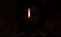 Burning candle illuminates the icon of Jesus Christ in the dark