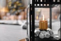 Burning candle in lantern against blurred background. Stylish interior element