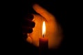 A burning candle at night, protected by the hand of a woman. Candle flame glowing on a dark background with free space for text.