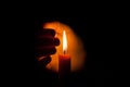 A burning candle at night, protected by the hand of a woman. Candle flame glowing on a dark background with free space for text. Royalty Free Stock Photo