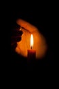 A burning candle at night, protected by the hand of a woman. Candle flame glowing on a dark background with free space for text.