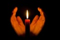 A burning candle at night, surrounded by the hands of a woman. Symbol of life, love and light, protection and warmth.