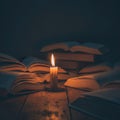 A burning candle among open books in a dark room. Royalty Free Stock Photo