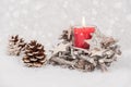 Burning candle and pine cone in the snow