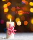 Burning candle with red bow, in snow, with defocussed fairy lights, bokeh in the background Royalty Free Stock Photo