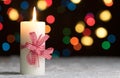 Burning candle with red bow, in snow, with defocussed fairy lights, bokeh in the background Royalty Free Stock Photo