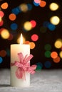 Burning candle with red bow, in snow, with defocussed fairy lights, bokeh in the background Royalty Free Stock Photo