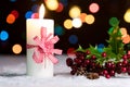 Burning candle with red bow, in snow, with defocussed fairy lights, bokeh