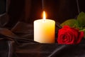 A burning candle and a red rose on a black cloth background. The concept of condolence and religion. Focus in the background Royalty Free Stock Photo