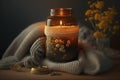 Burning candle in small amber glass jar, flowers of gypsophila and stack knitted seasin sweaters Cozy lifestyle, hygge concept.