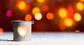 Burning candle, in snow, with defocussed fairy lights, bokeh in the background, Festive Christmas background Royalty Free Stock Photo