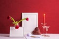 Burning candle, writing materials, tulips in a vase, white photo frames, iron heart on a red background Royalty Free Stock Photo