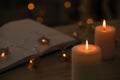 Burning candles, festive lights and open book in darkness, closeup. Space for text Royalty Free Stock Photo