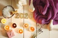 Burning candles illuminate the spa set and gold numbers 2020 on a white plank background with a purple cloth