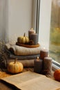 Burning candles, open book and stack of soft sweaters on windowsill. Autumn atmosphere Royalty Free Stock Photo