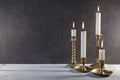 Burning candles in vintage metal candlesticks on white wooden table against dark stone background with copy space. Royalty Free Stock Photo