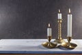 Burning candles in vintage metal candlesticks on white wooden table against dark stone background with copy space.