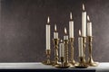 Burning candles in vintage metal candlesticks on white wooden table against dark stone background with copy space.