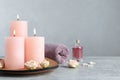 Burning candles, roses, essential oil and towel on grey table