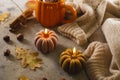 Burning candles shape of pumpkin, mug with autumns drink, leaves and cinnamon. Autumn mood, hygge atmosphere