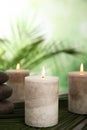 Burning candles and spa stones with palm leaf on table against blurred green background Royalty Free Stock Photo