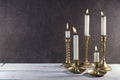 Burning candles in vintage metal candlesticks on white wooden table against dark stone background with copy space.