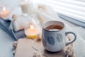 Burning candles and white sweaters on windowsill. Cozy autumn and winter concept, window with blinds Royalty Free Stock Photo