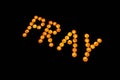 Burning candles. Word Pray made with burning yellow candles on black background.