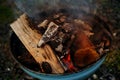 burning fire in compact grill, wood logs engulfed red flames, closeup of metal grill on burning coals, aromatic smoke rises