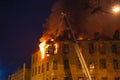 Burning house at night, roof of building in flames and smoke, firefighter on crane extinguishes fire with water from hose Royalty Free Stock Photo