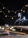 Burning incense stick and smoke, wooden base and wooden storage box for sticks on dark black background with semi precious stones Royalty Free Stock Photo