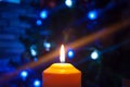 A burning orange candle on a dark background with blue lights - a Christmas New Year`s eve divination mystic esoteric