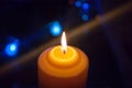 A burning orange candle on a dark background with blue lights - a Christmas New Year`s eve divination mystic esoteric