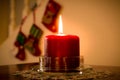 Burning red candle with Christmas stockings in the background Royalty Free Stock Photo