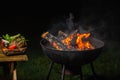 Burning round brazier and grilled vegetables. Evening time. Dark background
