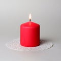 Burning single thick pink aromatic candle on white openwork paper napkin on gray background closeup view