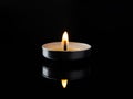 Burning tea light candle in the darkness. Lit candle is reflected in a black glossy surface. Focus on a single candlelight against Royalty Free Stock Photo