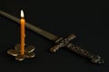 Burning wax candle on bronze candlestick in shape of flower and dagger-stylet replica with bronze handle adorned with medieval