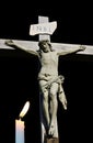 Lit candle shining in front of cement statue of Jesus