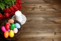 Burning white wax candle on openwork napkin, birds nest with multicolored easter eggs and bouquet of red tulip flowers on dark