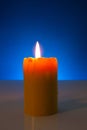 Burning yellow candle against blue background