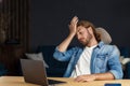 Burnout and overwork concept. Tired businessman working overtime in office with laptop. Stressed young handsome curly