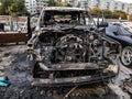 A burnt car after a fire or an accident in a parking lot covered with rust and black coal with scattered spare parts around.