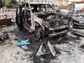 A burnt car after a fire or an accident in a parking lot covered with rust and black coal with scattered spare parts around.