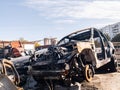 A burnt car after a fire or an accident in a parking lot covered with rust and black coal with scattered spare parts around.