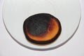 Burnt little pancake lies on the edge of a white plate, which is located on a white background