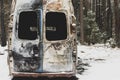 A burnt-out minivan stands near the forest in winter